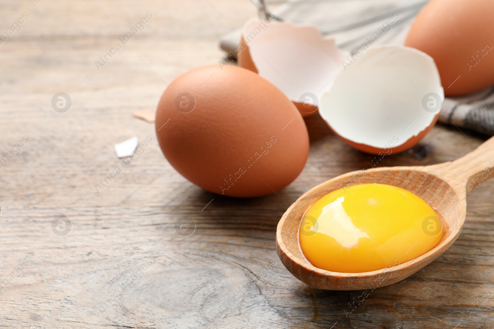 Photo of Raw chicken eggs and spoon with yolk on wooden table, space for text