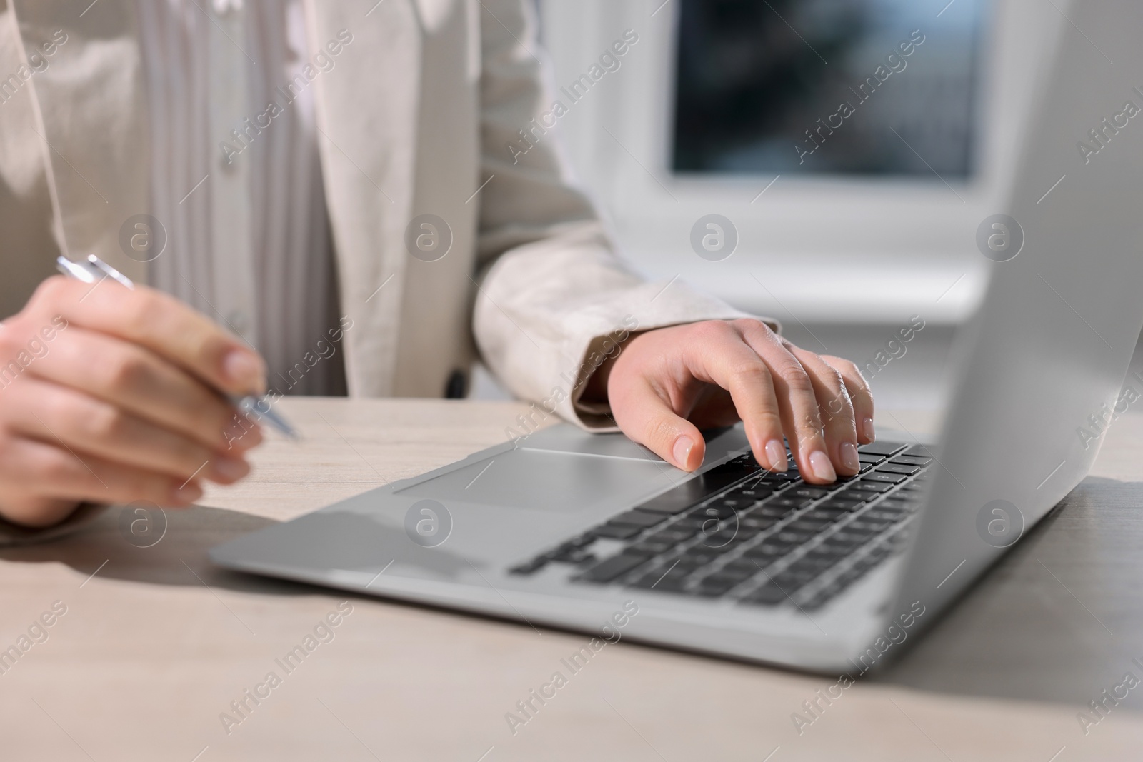 Photo of Woman with pen working on laptop at wooden table, closeup. Electronic document management