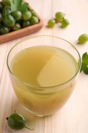 Photo of Tasty gooseberry juice in glass on wooden table, closeup