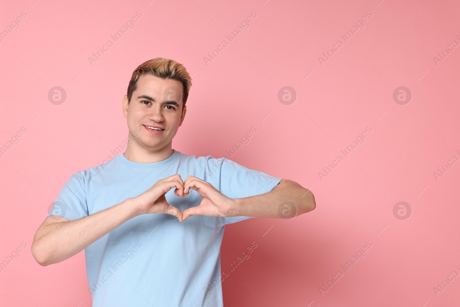 Photo of Young man showing heart gesture with hands on pink background, space for text