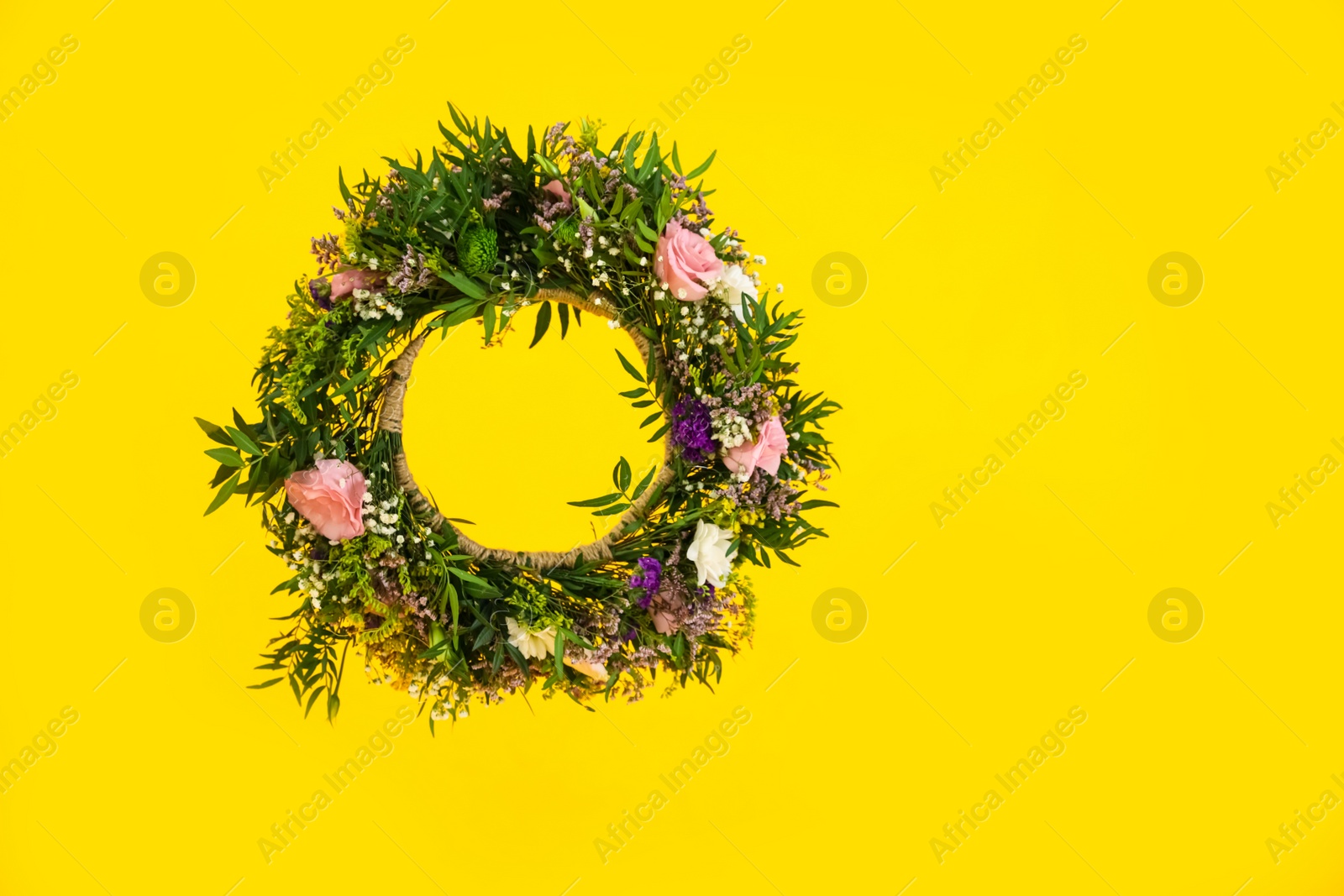 Photo of Wreath made of beautiful flowers hanging on yellow background. Space for text