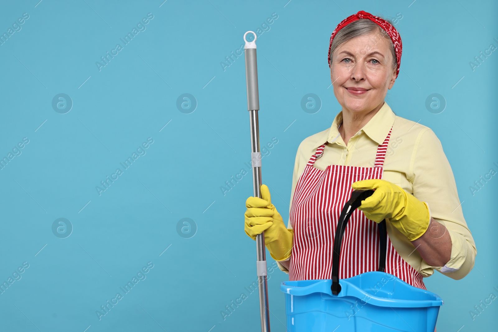 Photo of Happy housewife with mop and bucket on light blue background, space for text