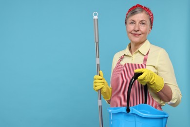 Happy housewife with mop and bucket on light blue background, space for text