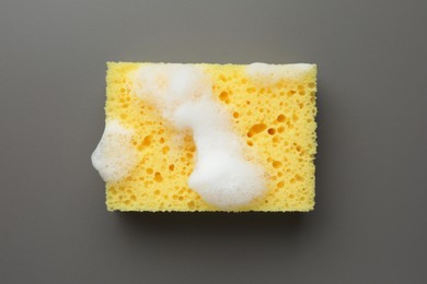 Yellow sponge with foam on grey background, top view