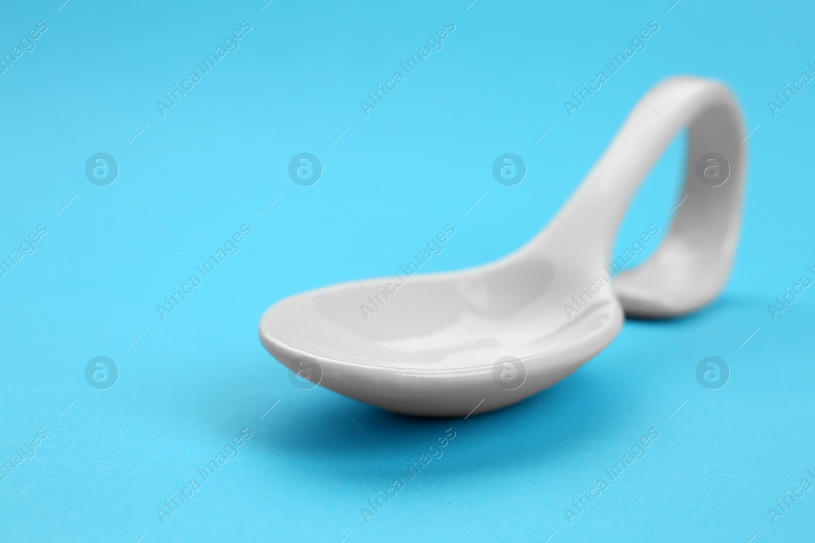 Photo of Clean empty ceramic appetizer spoon on blue background, space for text