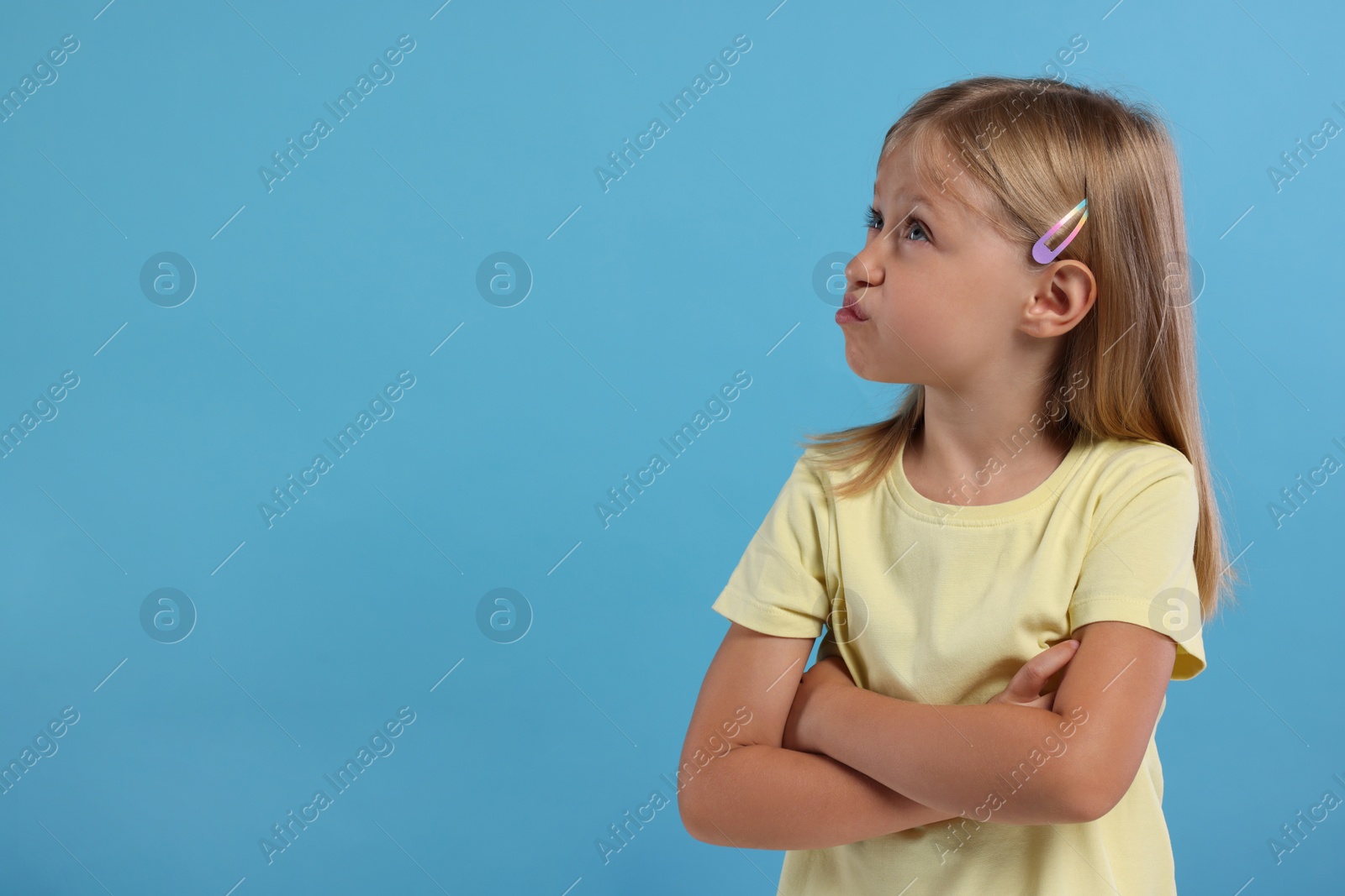 Photo of Resentful girl with crossed arms on light blue background. Space for text