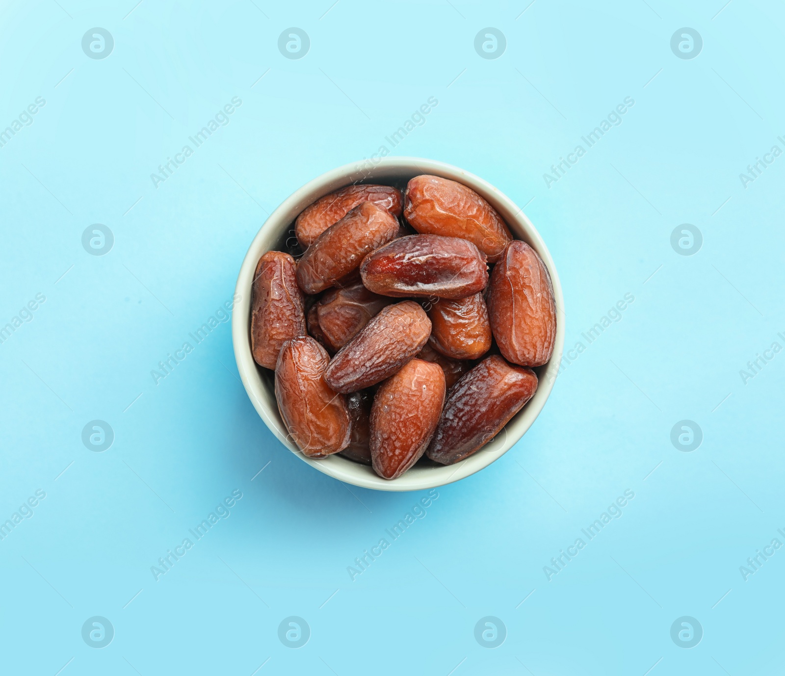 Photo of Bowl with sweet dried date fruits on color background, top view