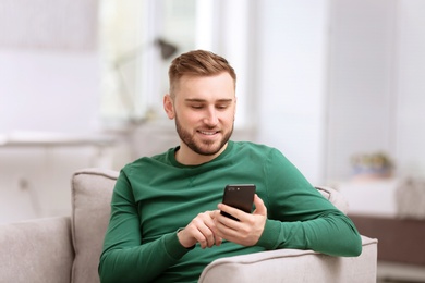 Photo of Portrait of confident young man with mobile phone in armchair