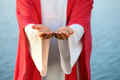 Photo of Jesus Christ reaching out his hands near water outdoors, closeup