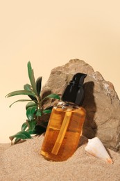 Bottle of serum, stone and green leaves on sand against beige background