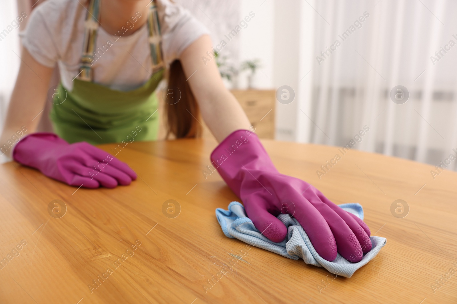 Photo of Woman with microfiber cloth cleaning wooden table in room, closeup