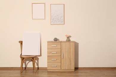 Wooden cabinet, decor and posters in room with beige wall