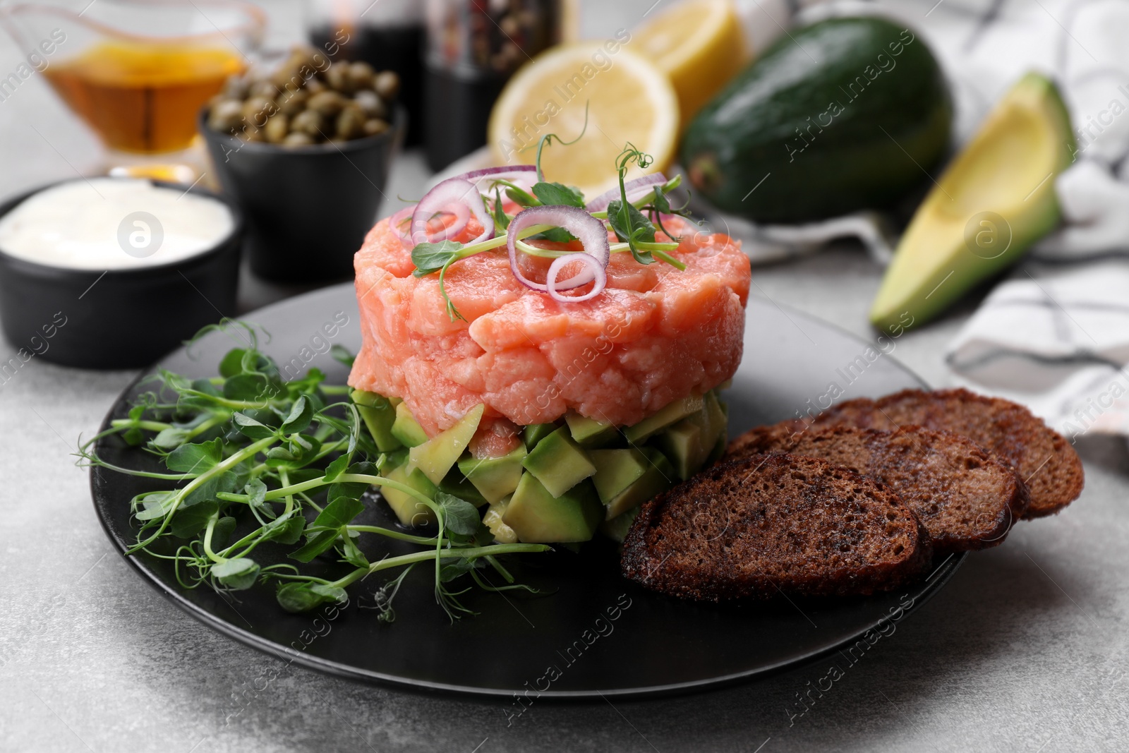 Photo of Tasty salmon tartare with avocado, microgreens and croutons on grey table, closeup