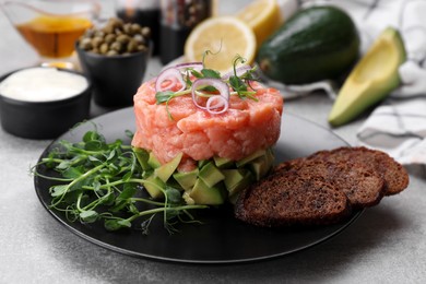 Tasty salmon tartare with avocado, microgreens and croutons on grey table, closeup