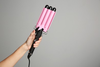 Photo of Woman holding triple curling hair iron on light grey background, closeup. Space for text