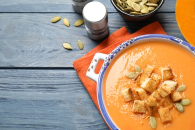 Photo of Tasty creamy pumpkin soup with croutons and seeds in bowl on blue wooden table, flat lay. Space for text