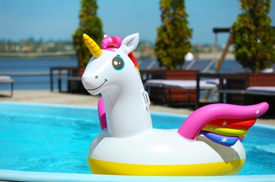 Photo of Funny inflatable unicorn ring floating in swimming pool on sunny day, outdoors