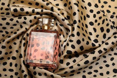 Photo of Luxury perfume in bottle on fabric with leopard pattern, above view