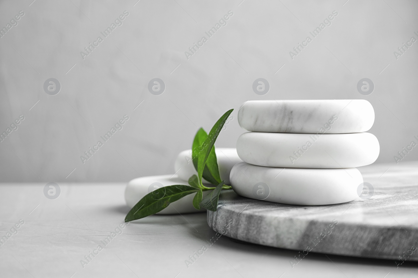 Photo of Board with spa stones and green leaves on grey table, space for text