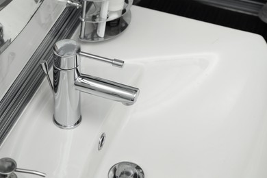 Photo of Clean white sink with shiny water tap in bathroom