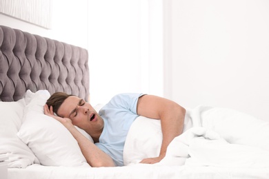 Young man yawning in bed with pillows at home
