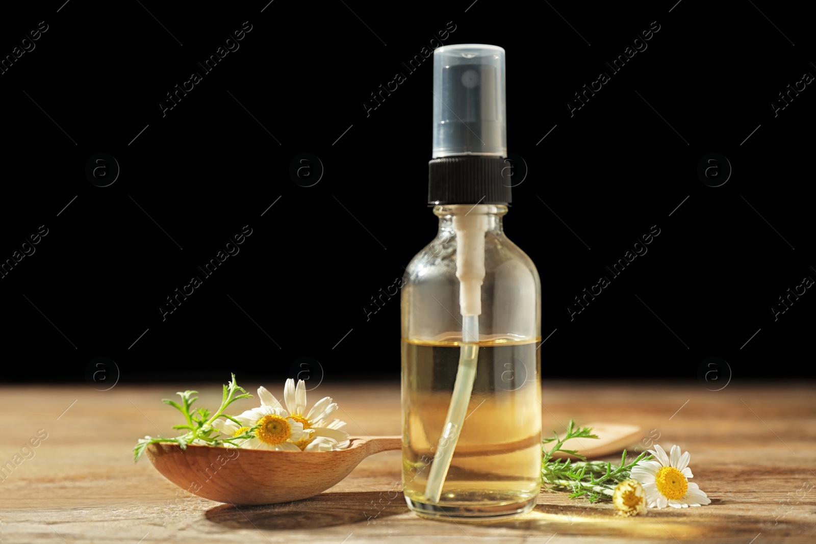 Photo of Bottle of chamomile essential oil and spoon with flowers on wooden table