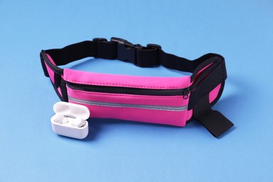 Photo of Stylish pink waist bag and earphones on light blue background