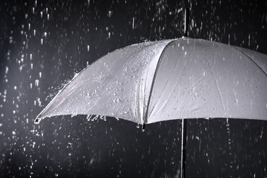 Photo of White umbrella under rain on dark background