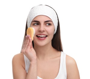 Young woman with headband washing her face using sponge on white background