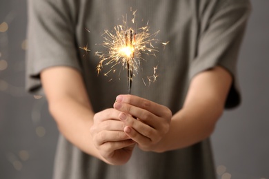 Woman holding burning sparklers against blurred lights, closeup