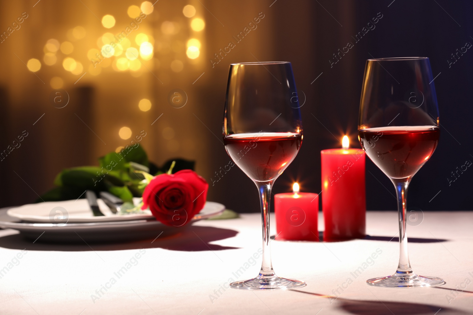 Photo of Beautiful table setting with glasses of wine, candles and rose against blurred lights. Romantic dinner for Valentine's day