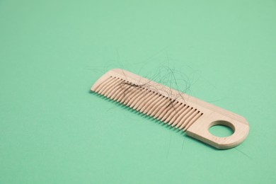 Photo of Wooden comb with lost hair on green background. Space for text