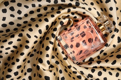 Photo of Luxury perfume in bottle on fabric with leopard pattern, top view