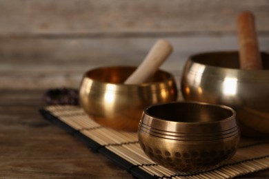 Photo of Golden singing bowls and mallets on wooden table, space for text