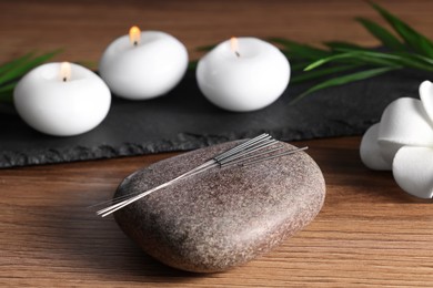 Photo of Stone with acupuncture needles and burning candles on wooden table