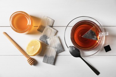 Photo of Tea bags, honey and lemon near cup of hot drink on white wooden table, flat lay