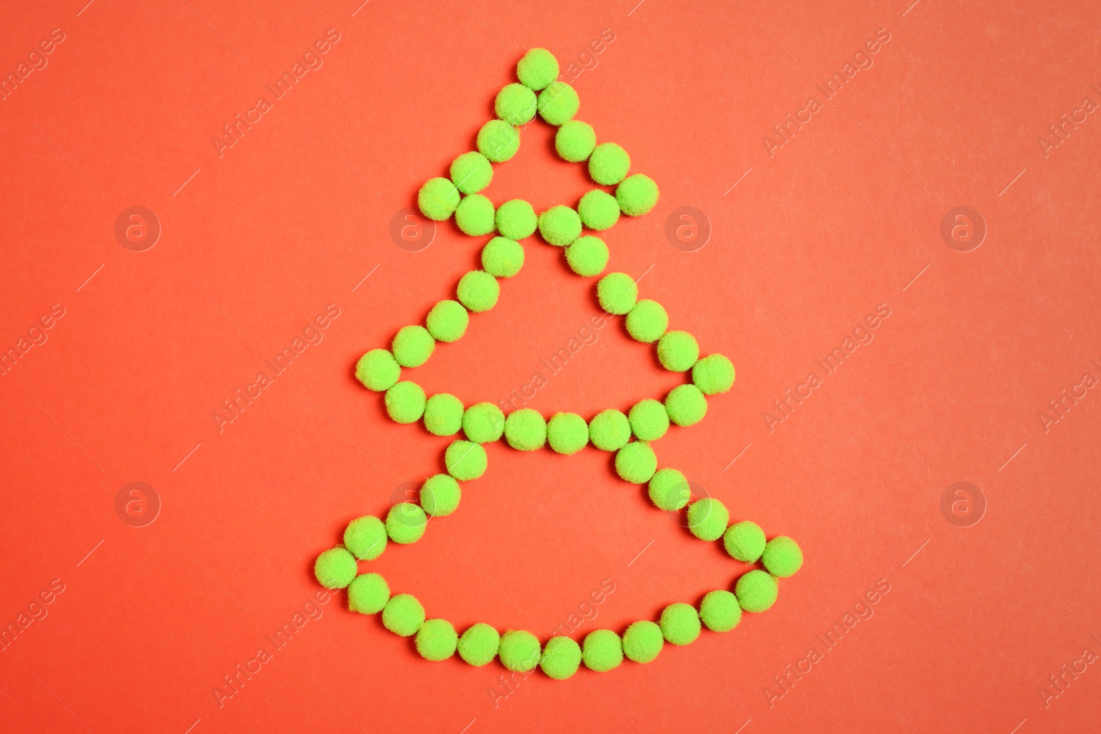 Photo of Christmas tree shape made with green fluffy balls on orange background, flat lay