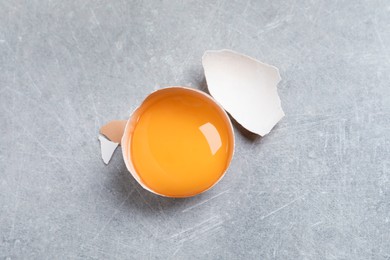Photo of Cracked eggshell with raw yolk on light grey table, top view