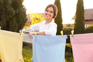Photo of Woman with basket drying clothes in backyard on sunny day