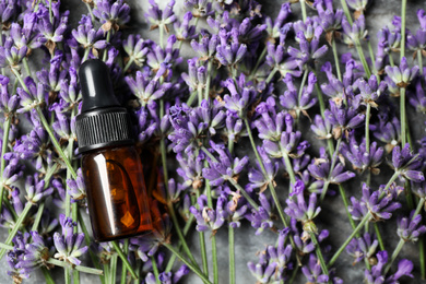 Photo of Bottle of essential oil on lavender flowers, flat lay