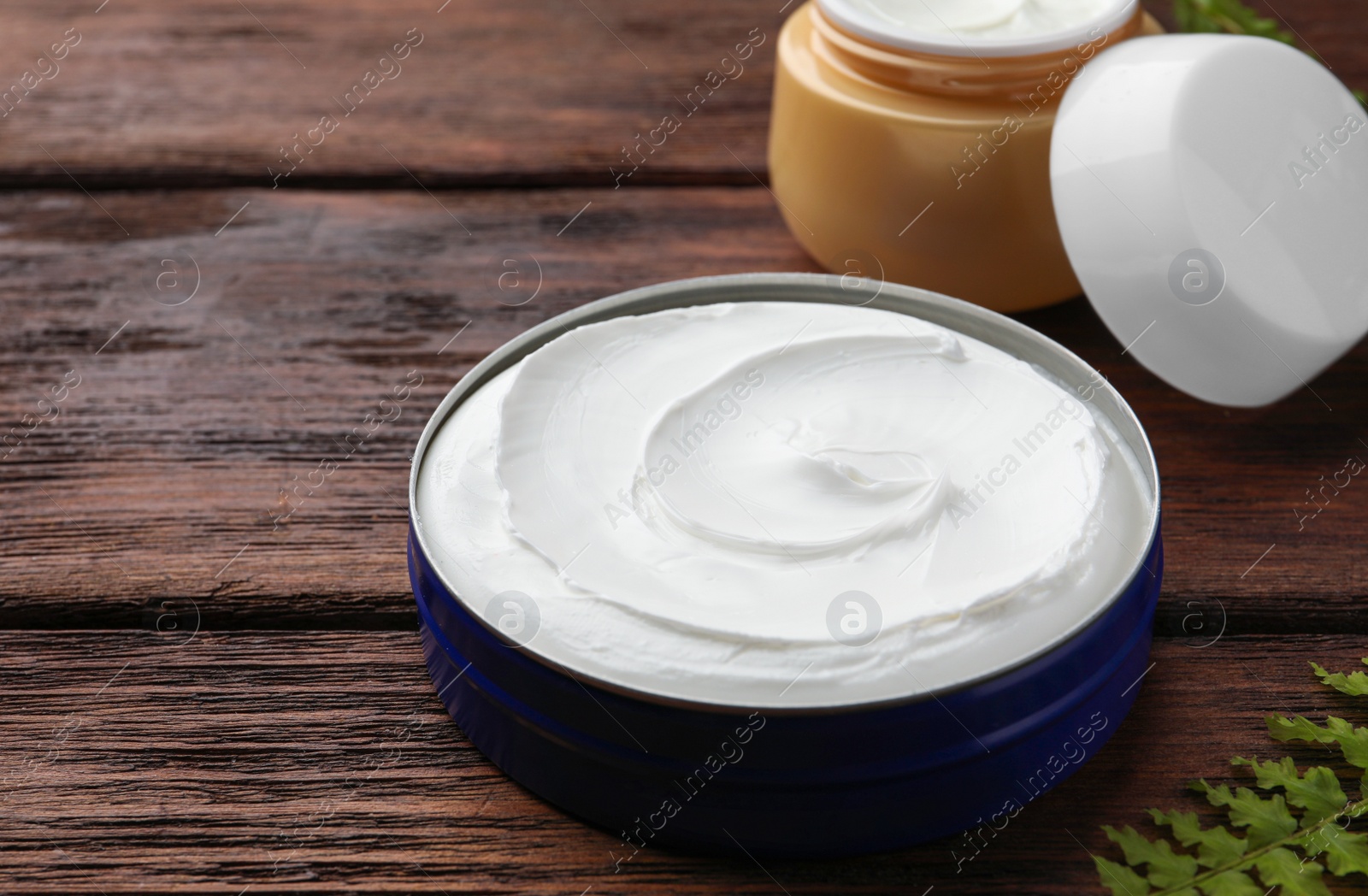 Photo of Jars of face cream and green plant on wooden table. Space for text