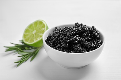 Photo of Ceramic bowl with black caviar on white wooden background