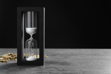 Hourglass and coins on table against black background. Time management