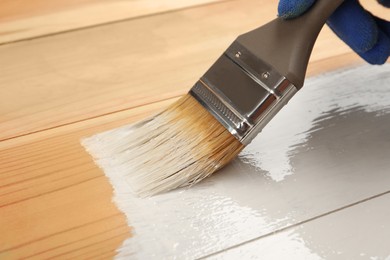 Photo of Worker applying white paint onto wooden surface, closeup