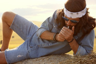 Photo of Hippie man smoking joint on hay bale in field
