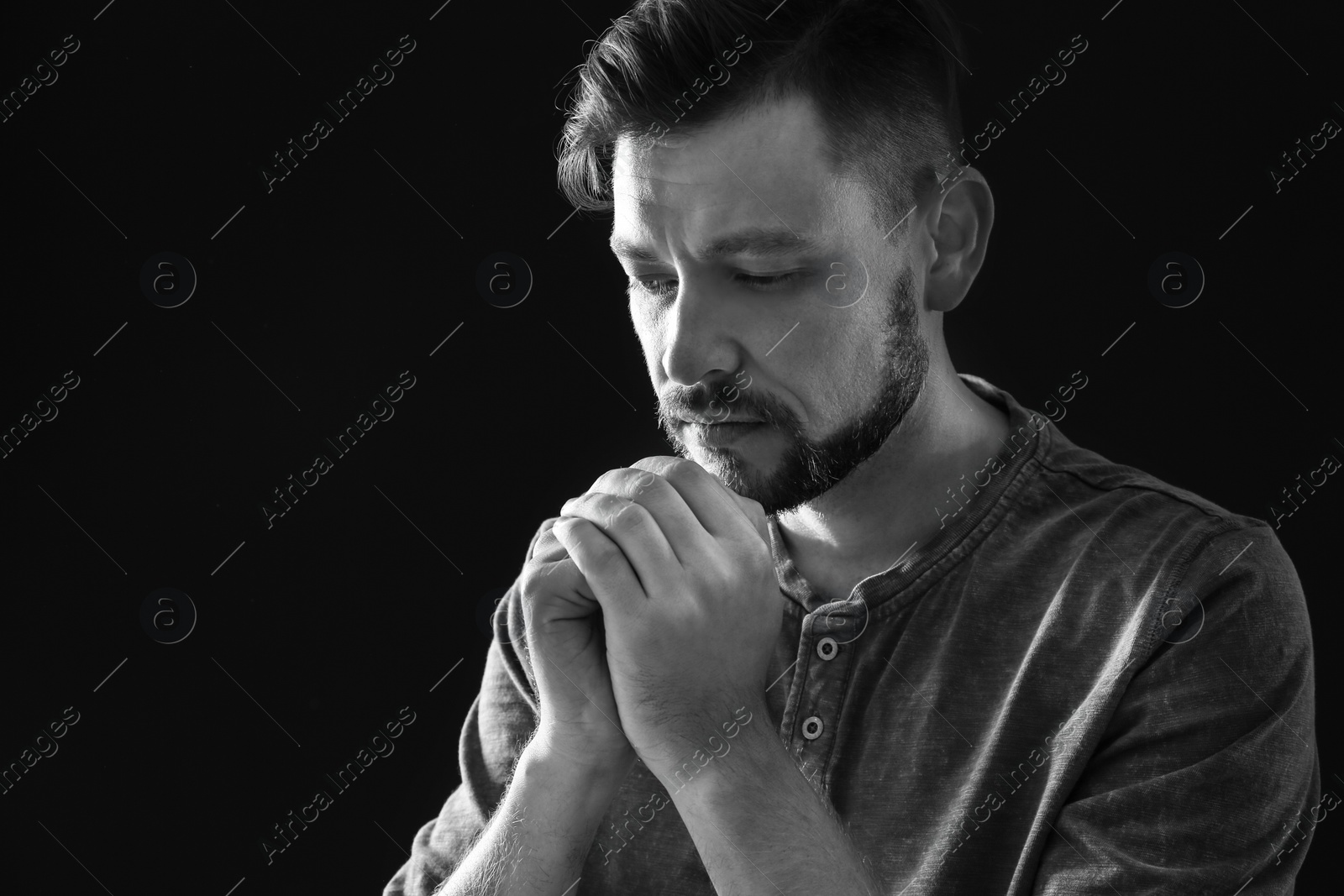 Photo of Man with hands clasped together for prayer on dark background, black and white effect. Space for text