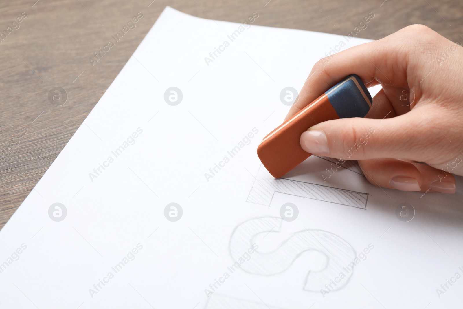 Photo of Woman erasing word on sheet of white paper at wooden table, closeup