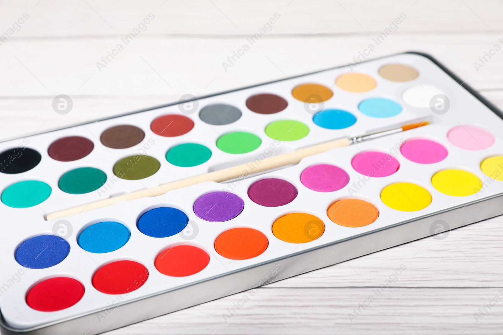 Photo of Watercolor palette with brush on white wooden table, closeup