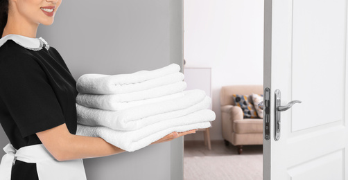 Image of Chambermaid with clean folded towels near door in hotel, closeup