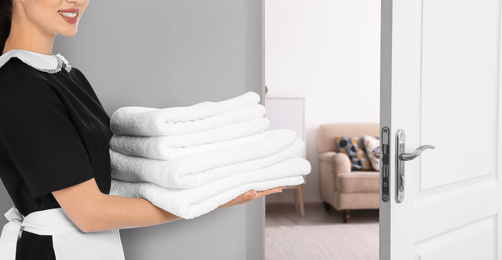 Chambermaid with clean folded towels near door in hotel, closeup